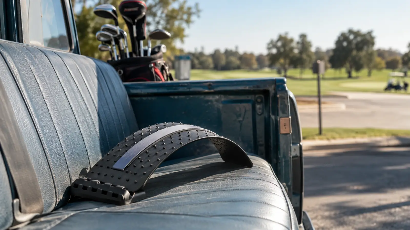 A back stretching device resting on the bench seat of a pickup truck parked at a golf course.